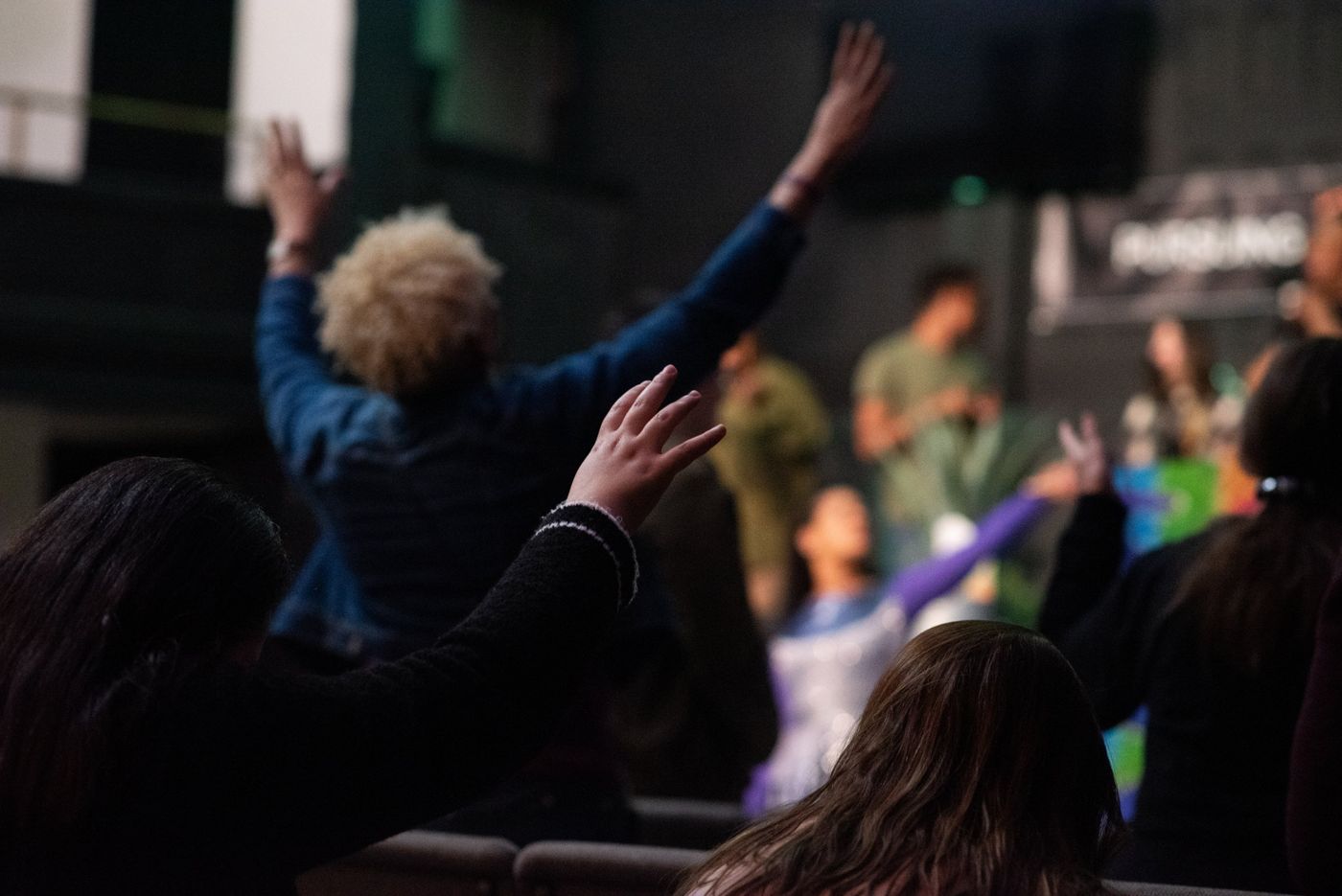 Hands raised across the room during worship, seen from behind