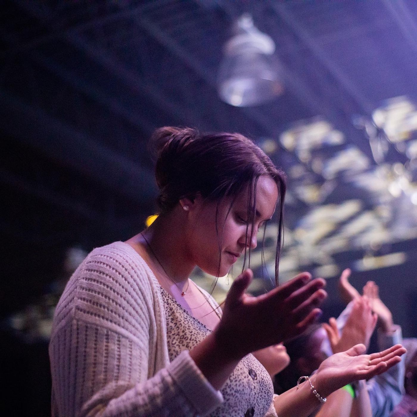 A young woman with her hands open and eyes down during worship